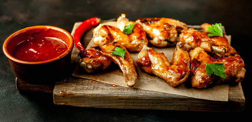 Grilled chicken wings in a barbecue sauce with parsley on a cutting board on a concrete table.