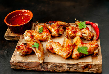 Grilled chicken wings in a barbecue sauce with parsley on a cutting board on a concrete table.