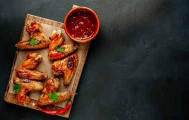 Grilled chicken wings in a barbecue sauce with parsley on a cutting board on a concrete table. Top view with copy space.