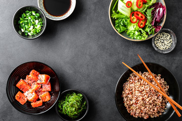 culinary background of poke bowl ingredients - brown rice, trout or salmon fillet, Chuka Seaweed Salad, sesame and fresh vegetables, top view, copy space, healthy food background