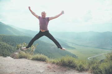 The young man jumps on a rock in the background of the valley, hands to the sides.