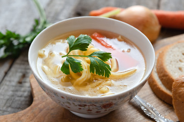 Chicken soup with noodles and carrot in white bowl.