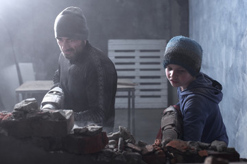 A man worker and his boy son child breaks a brick wall with a jackhammer, builds and repairs his...