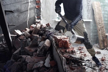 A man handyman breaks a brick wall with a hammer, builds and repairs his house