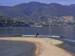 a young couple observes the beauty of the lake from a sand spit. Como - Italy