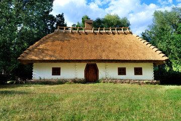 Fototapeta na wymiar Old traditional Ukrainian rural house with thatched roof and wicker fence in the garden