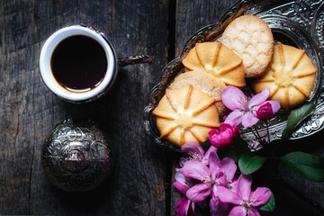 tasty coffee in a traditional Turkish cup and butter cookies and a sprig of pink flowers on a wooden table - flat lay food background