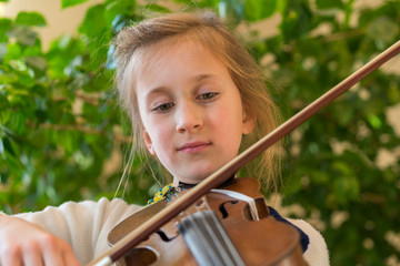 Close up of a child playing violin on green background. Portrait of girl with string and playing...