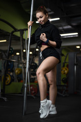 Fototapeta na wymiar Girl posing in the gym, showing off her body, holding a barbell