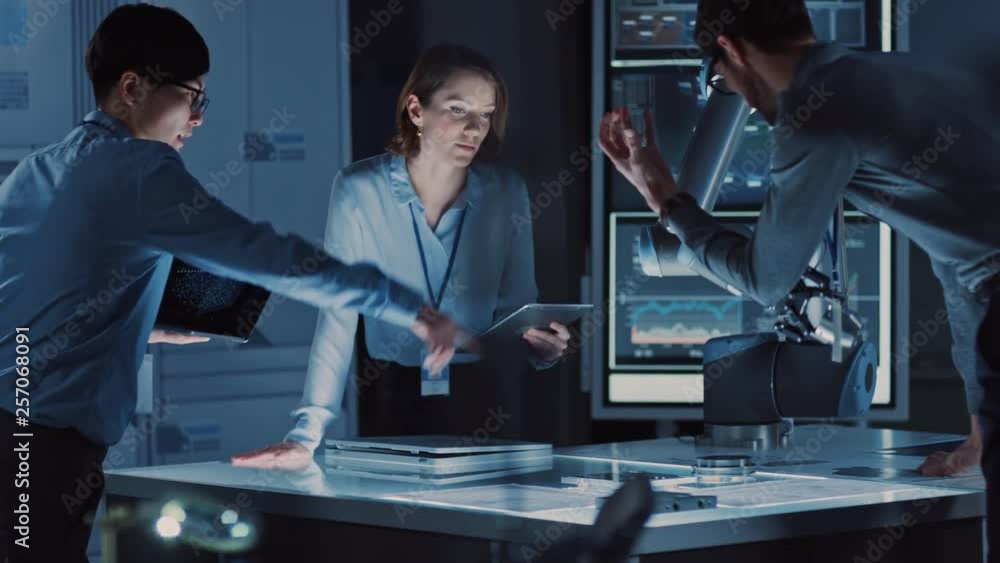 Poster diverse team of engineers with laptop and a tablet analyse and discuss how a futuristic robotic arm 