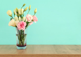 summer bouquet of white and pink flowers in the vase over wooden table and pastel mint background