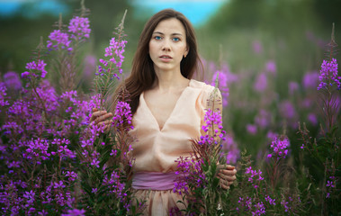 beautiful woman with brunette hair in light clothes posing in flower field on background