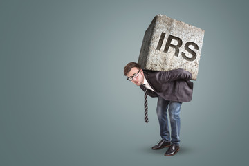 Businessman carrying a heavy stone with the letters IRS on it  - obrazy, fototapety, plakaty