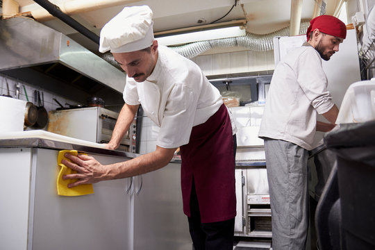 two people, young chef in kitchen cleaning cabinets, after closing restaurant.