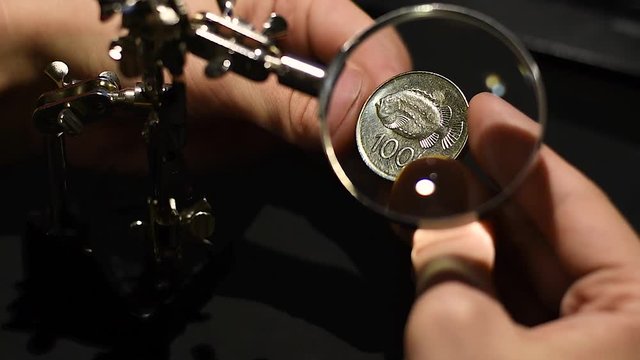 A man inspects the Icelandic krone coin under a magnifying glass