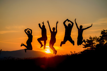 group of cheerful friends are jumping together at amazing sunset in the background of the mountains