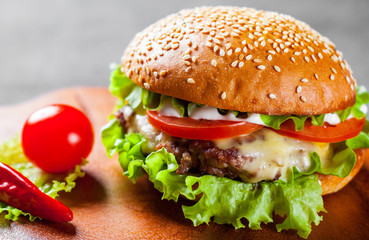 burger with meat, cheese and vegetables on wooden board