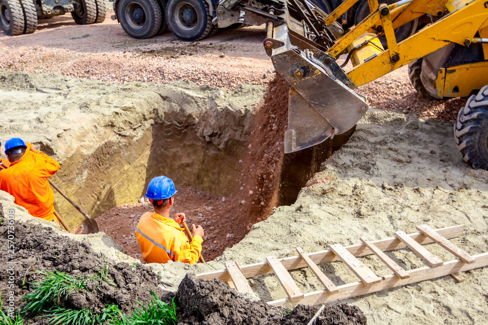 Wall mural Backhoe is pouring gravel in trench at construction site