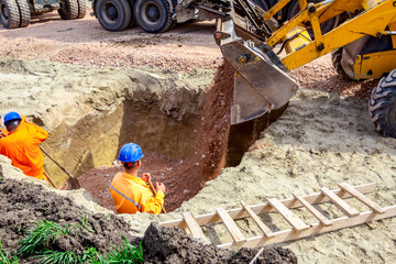 Backhoe is pouring gravel in trench at construction site