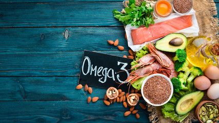 Foods containing omega 3. Vitamin Healthy foods: avocados, fish, shrimp, broccoli, flax, nuts, eggs, parsley. Top view. Free space for your text. On a blue wooden background.