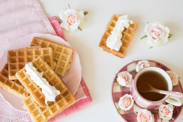 flat lay tea time with Belgian waffles with cream, on pink napkin, white table