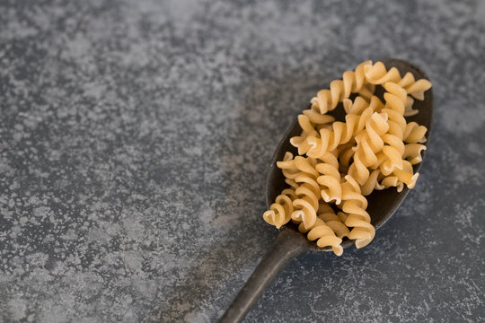 heap spiralli pasta on dark vintage spoon, concrete kitchen dresser, space for text
