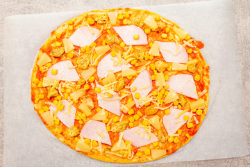 Raw Hawaiian pizza on parchment on stone background close up top view.