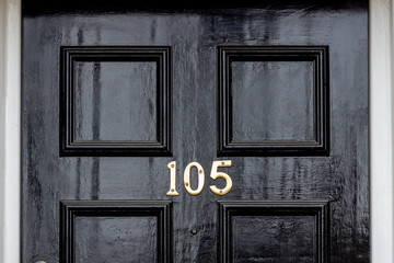 House number 105 with the one hundred and five in silver on the middle cross frame of a panelled wooden house door
