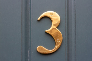 House number three in bright bronze shiny metal on a blue grey house door