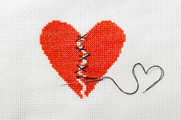 The broken red heart is threaded with black threads. Heart embroidered on white cloth.