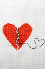 The broken red heart is threaded with black threads. Heart embroidered on white cloth.