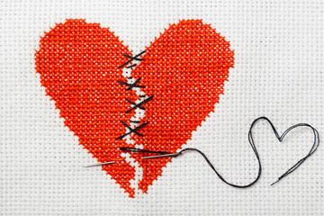 The broken red heart is threaded with black threads. Heart embroidered on white cloth.