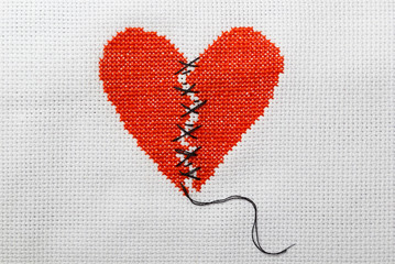 The broken red heart is threaded with black threads. Heart embroidered on white cloth.