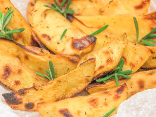 Perfect roasted potato wedges with spices and herbs on wood board. Closeup