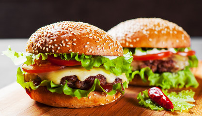 two burger with meat, cheese and vegetables on wooden board