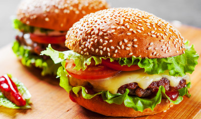 two burger with meat, cheese and vegetables on wooden board