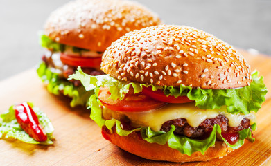 two burger with meat, cheese and vegetables on wooden board