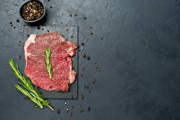 Raw beef flank steak on a stone Board with rosemary. Black background, top view, space for text