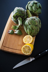 Fresh artichokes on wooden cutting board with lemons