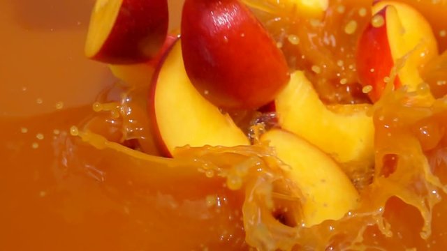 Slices of peach fall into juice with beautiful splashes in slow motion