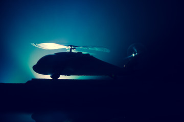 Silhouette of military helicopter ready to fly from conflict zone. Decorated night footage with helicopter starting in desert with foggy toned backlit. Selective focus.