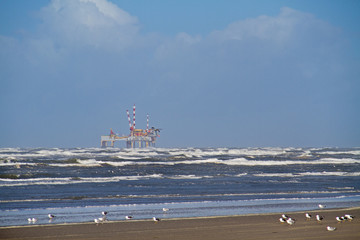 Offshore production platform near the Dutch island Ameland, beach, breaking waves and gulls in the foreground 