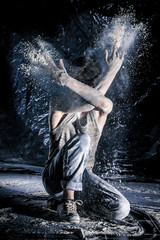 cool dirty сhinese guy dancer in style of bboying doing complex tricks on floor in Studio filled with flour on black background. concept of space dance on surface of planet moon