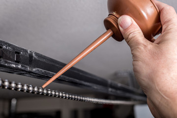 Oil from a metal can is applied to the top of a chain on a garage door opener