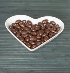 Nuts arranged in heart shape on background. Food image close up candy, chocolate milk, extra dark almond nuts. Love Texture