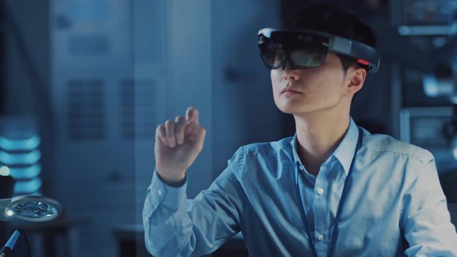 Professional Japanese Development Engineer is Working in a AR Headset, Moving Virtual Pieces Around and Looking at Graphics in the High Tech Research Laboratory with Modern Computer Equipment