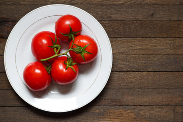 Copy space in right side of wooden background with washed tomatoes on white plate.