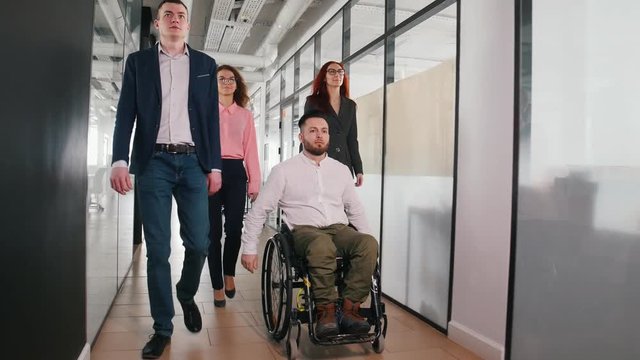 A successful business people walking through the corridor. A man in a wheelchair going first of the group