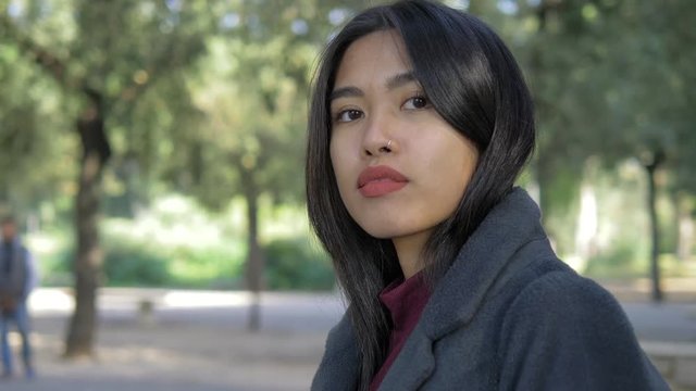 Serious confident beautiful asian woman turning,staring at camera in the park