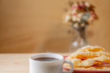 Food and dessert. Crackled crispy cookies with sugar on a plate and a cup of coffee on a wooden table. Copy space. Blurry background with bouquet of flowers in a vase. Soft focus.